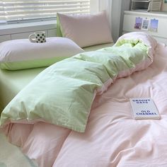 a book is laying on the bed with pink and green sheets in front of it