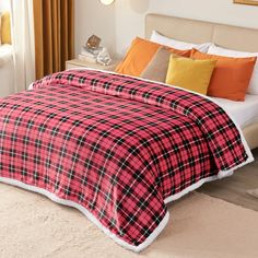 a red and black plaid comforter on a white bed with orange, yellow, and brown pillows