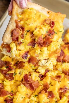 a person holding up a slice of pizza with scrambled eggs and bacon on it,