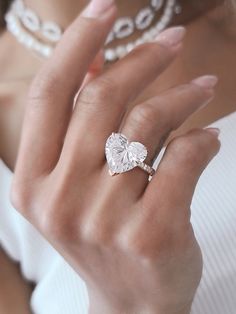 a close up of a person wearing a ring with a heart shaped diamond on it