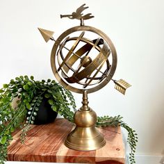 an antique brass globe with arrows and bottles on it sitting on top of a wooden table