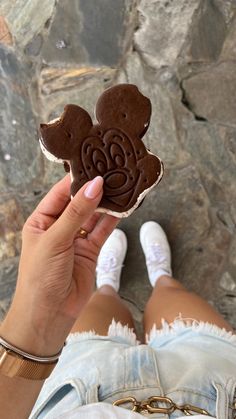 a person holding up a chocolate mickey mouse cookie in front of their face and feet