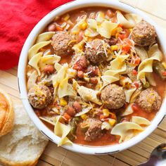 a white bowl filled with pasta and meatball soup next to a piece of bread