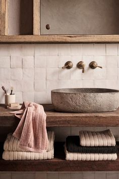 a bathroom sink sitting under a mirror next to a wooden shelf with towels on it