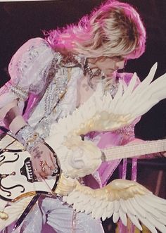 a woman with pink hair is playing an electric guitar and has wings around her neck