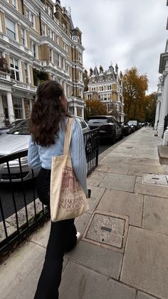 a woman is walking down the sidewalk carrying a shopping bag and looking at some cars