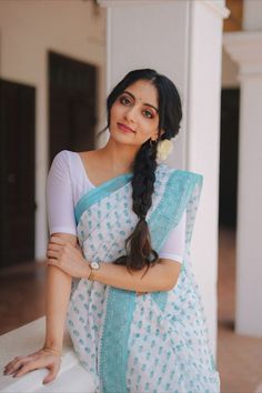 a woman in a blue and white sari with her arms crossed, leaning on a wall