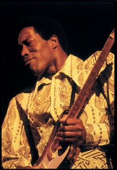 a man holding a guitar in his right hand and wearing a shirt with paisley patterns on it