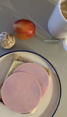 two slices of bread with ham on them next to a cup of coffee and an apple