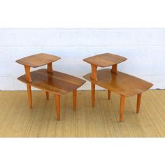 two wooden end tables sitting on top of a floor next to a wall with a white brick wall behind them