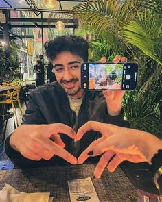 a man sitting at a table with his hands in the shape of a heart while taking a selfie