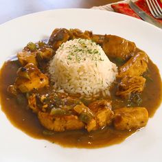 a white plate topped with rice and meat covered in gravy on top of a table