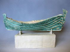 a sculpture of a long boat on a wooden stand with blue background and white base