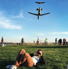 a man laying in the grass with an airplane flying overhead