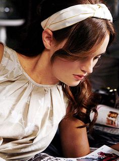 a woman sitting down reading a book with a headband on her head and looking at the camera