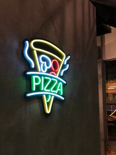 a neon sign on the side of a building that says pizza and is lit up