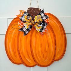 an orange pumpkin shaped door hanger with a black and white checkered bow on it