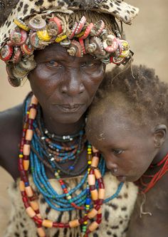 an african woman holding a child with beads on her head and jewelry around her neck