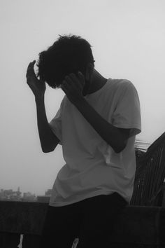 a man sitting on top of a wooden bench holding his hands to his face while wearing a white t - shirt