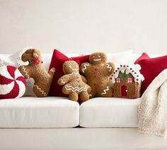 three gingerbread men sitting on a white couch with red and white throw pillows in front of them