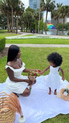 two women in white dresses are sitting on the grass and one woman is holding flowers