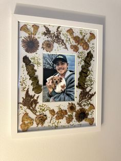 a photo frame with an image of a man holding a dog in his lap and flowers on the wall