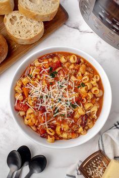 a white bowl filled with pasta and cheese on top of a counter next to bread