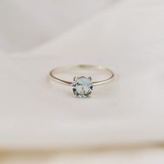 a white gold ring with an aqua blue topazte in the center on a white cloth