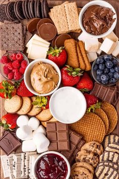 an assortment of snacks and desserts are arranged on a wooden board with chocolate, strawberries, crackers, marshmallows, raspberries