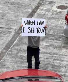 a man holding a sign that says when can i see you?