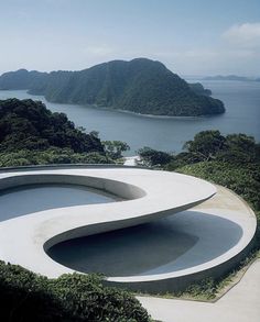 an unusual concrete building in the middle of some hills and water with mountains in the background