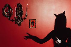 a woman standing in front of a red wall with her shadow on the wall and candles