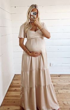 a pregnant woman taking a selfie in front of a white wall wearing a dress