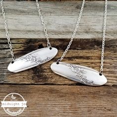 two silver necklaces sitting on top of a wooden table