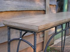 an iron and wood table sitting on the side of a building next to a window