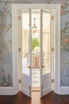 an open door leading to a dining room with floral wallpaper on the walls and wooden floors