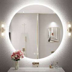 a bathroom with a round mirror on the wall above it and flowers in a vase