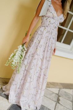 a woman in a long dress holding a bouquet of flowers standing next to a building