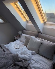 an unmade bed sitting under two windows in a room with slanted ceilinging