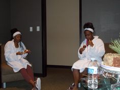 two women in white robes sitting on couches eating cake and drinking water from cups