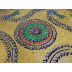 an intricately designed wooden table top with green and orange designs on the surface,