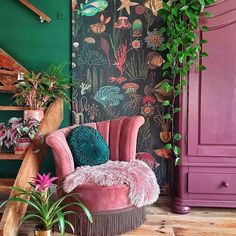 a pink chair sitting in front of a green wall with plants and other decorations on it