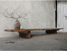 a wooden bench with two vases on top of it next to a white wall