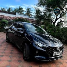 a black car is parked in front of a brick driveway with trees and bushes behind it