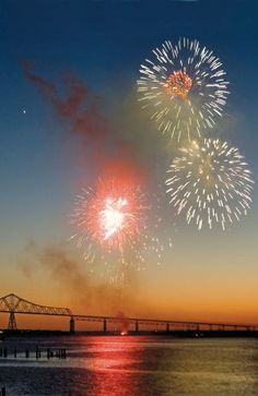 fireworks are lit up over the water and bridge