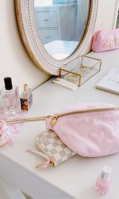 a pink purse sitting on top of a desk next to a mirror and perfume bottle