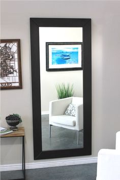 a mirror with a chair in front of it and pictures on the wall behind it