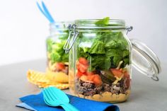 two mason jars filled with salad on top of a table next to a blue napkin