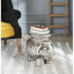 a silver elephant shaped table with books on top and a chair in the back ground