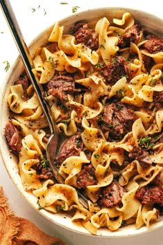 a bowl filled with pasta and meat on top of a white table next to a wooden spoon